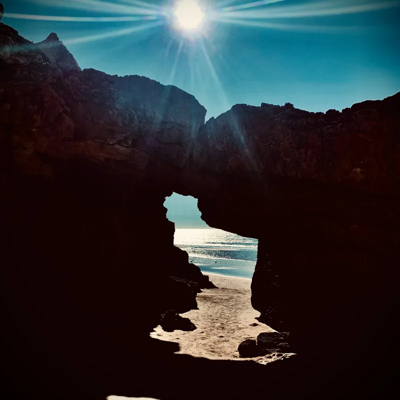 Sun shining through a natural rock arch above a Lagos beach